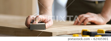 Carpenter man grinds wooden sheet in workshop 62485901