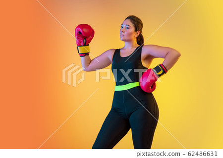 Young caucasian plus size female model's training on gradient orange background Young caucasian plus size female model's training on gradient orange background 62486631