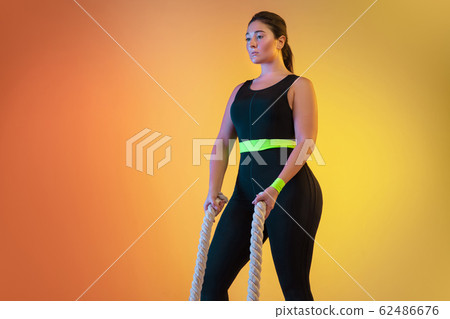 Young caucasian plus size female model's training on gradient orange background Young caucasian plus size female model's training on gradient orange background 62486676
