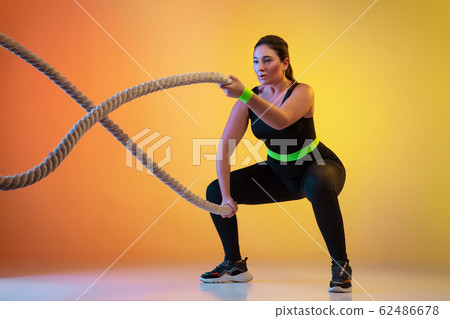 Young caucasian plus size female model's training on gradient orange background 62486678
