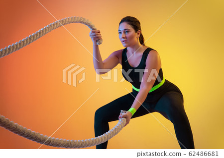 Young caucasian plus size female model's training on gradient orange background 62486681