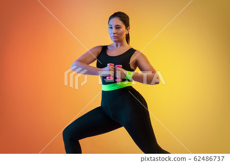 Young caucasian plus size female model's training on gradient orange background 62486737