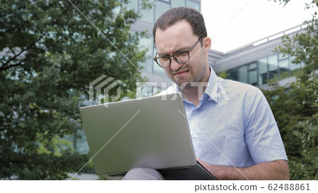 Comic emotion. Young businessman with disgusted emotion holding laptop in a park. 62488861
