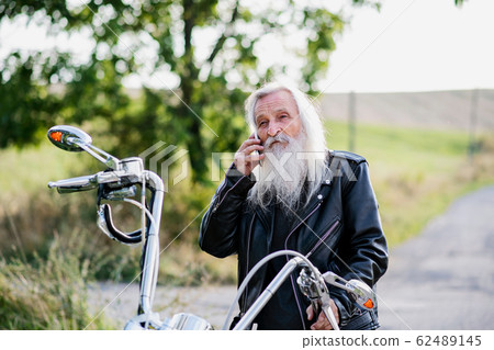 Senior man traveller with motorbike in countryside, using smartphone. Senior man traveller with motorbike in countryside, using smartphone. 62489145