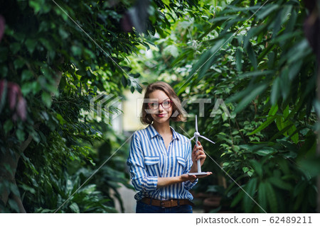 Young woman with windmill model standing in botanical garden. Young woman with windmill model standing in botanical garden. 62489211