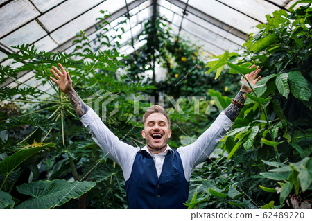 Young man standing in botanical garden, arms stretched. 62489220