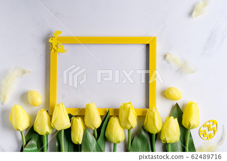 Flat Lay of Easter Eggs with tulips and yellow photo frame on stone marble background. Easter background or easter concept. Flat Lay of Easter Eggs with tulips and yellow photo frame on stone marble background. Easter background or easter concept. 62489716