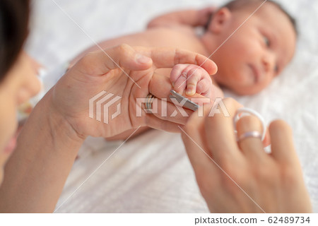 Baby getting fingernails cut while sleeping by his Baby getting fingernails cut while sleeping by his 62489734