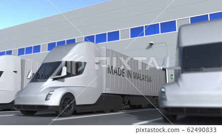 Modern semi-trailer trucks with MADE IN MALAYSIA text being loaded or unloaded at warehouse. Malaysian business related 3D rendering 62490833