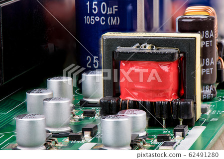 Close-up of a transformer with red isolation surrounded by capacitors. 62491280