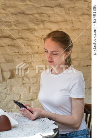 Girl sits at table and holds the phone. Student, 62491886