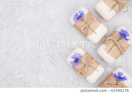 Handmade natural soap set border decorated with craft paper, scourge and blue cornflowers on gray stone backgroun . Organic cosmetics, zero waste, eco friendly concept. Top view Flat lay Copy space 62498176
