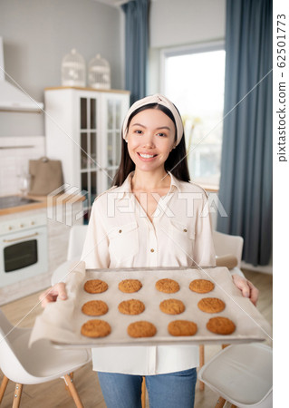 Woman with baking tray standing at home. Woman with baking tray standing at home. 62501773