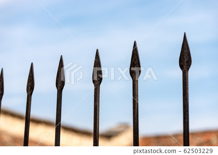 Wrought iron fence with sharp points on blue sky with clouds 62503229