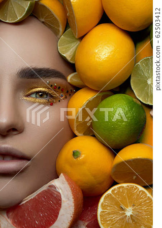 beautiful fashion professional model with bright makeup on a bright photo is lying with his mouth open on a background of fruit, lemon and lime citrus. High End retouch. Close up portrait beautiful fashion professional model with bright makeup on a bright photo is lying with his mouth open on a background of fruit, lemon and lime citrus. High End retouch. Close up portrait 62503412