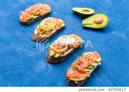 Sandwiches with smoked salmon, eggs, sauce and avocado on blue background. Concept of breakfast and healthy nutrition. 62509617