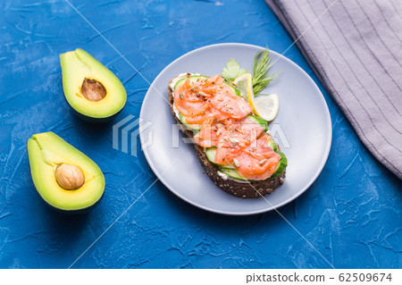 Sandwich with smoked salmon and cucumber on blue background with avocado, top view. Concept for healthy nutrition. Sandwich with smoked salmon and cucumber on blue background with avocado, top view. Concept for healthy nutrition. 62509674