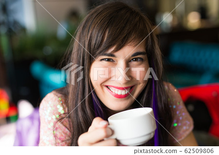 Portrait of young stylish trendy woman with multi-coloured strand in hair sits in cafe with cup of tea 62509806