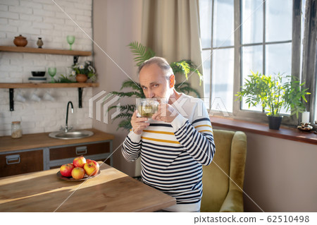 Bearded grey-haired man in a striped sweater having tea at home Bearded grey-haired man in a striped sweater having tea at home 62510498