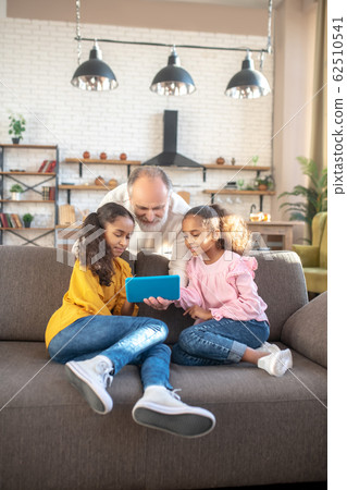 Two dark-skinned girls sitting on the sofa and watching a video Two dark-skinned girls sitting on the sofa and watching a video 62510541