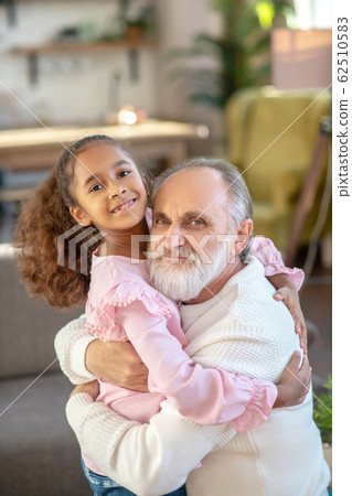 Grey-haired man hugging his cute granddaughter and looking happy 62510583