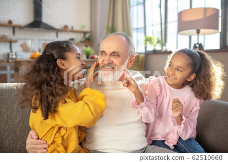 Bearded grey-haired man in a white shirt feeling amazing spending time with granddaughters 62510660