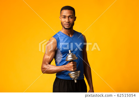 African bodybuilder pumping up biceps with dumbbells at gym 62515054