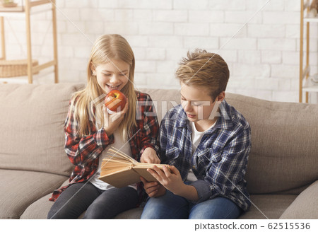Brother And Sister Reading Book Sitting On Sofa At Home Brother And Sister Reading Book Sitting On Sofa At Home 62515536