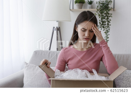 Upset woman customer unpacking delivered cardboard parcel 62515623