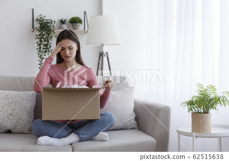 Negatively surprised girl sitting on coach and looking into cardboard box 62515638