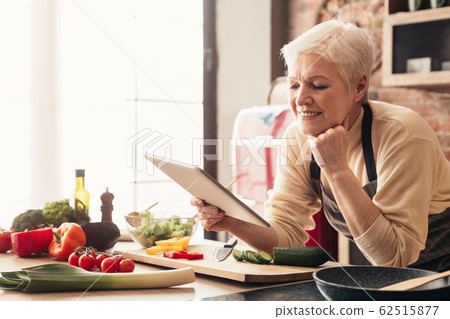 Elderly woman using digital tablet in kitchen, checking cooking recipes 62515877