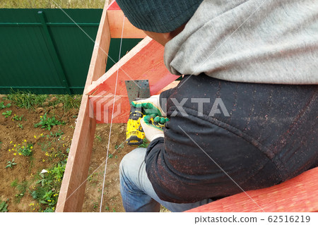 A man fastens two wooden beams with a self-tapping A man fastens two wooden beams with a self-tapping 62516219