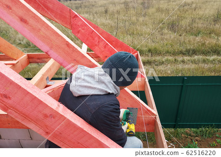 A man fastens two wooden beams with a self-tapping A man fastens two wooden beams with a self-tapping 62516220