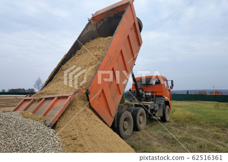 A dump truck unloads sand at a construction site. A dump truck unloads sand at a construction site. 62516361