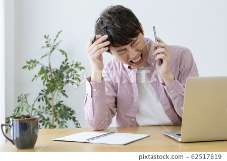 A man holding his head while talking on a smartphone 62517819