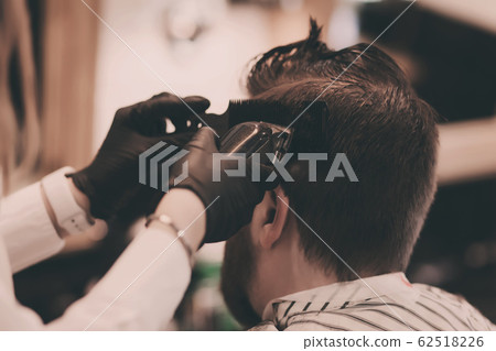 Barber in black gloves cuts a man's hair 62518226