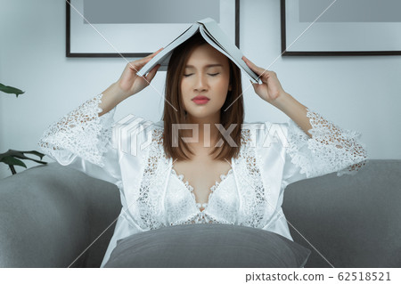 Woman holding her book over her head being tired of reading and sleepy 62518521