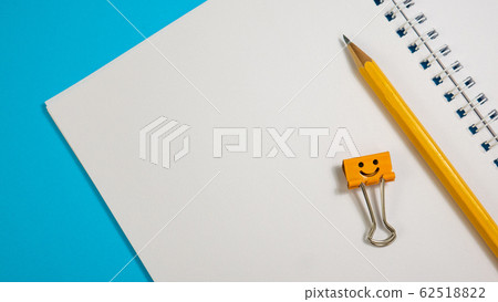 Notepad with Pencils and Yellow and Blue Binder Clip on Blue Background Notepad with Pencils and Yellow and Blue Binder Clip on Blue Background 62518822