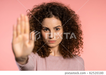 No, never, pretty curly woman disliking and rejecting gesture by stop palm sign. Portrait of young successful confident girl isolated on pink background. 62520180