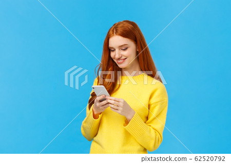 Conversation, messaging and people concept. Redhead cute carefree girl enjoy browsing online, picking new dress internet store, shopping using smartphone, smiling found excellent choice, order Conversation, messaging and people concept. Redhead cute carefree girl enjoy browsing online, picking new dress internet store, shopping using smartphone, smiling found excellent choice, order 62520792