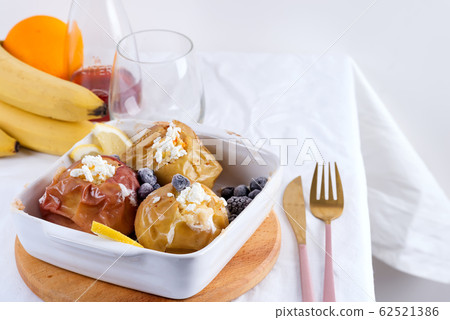 Baked apples with blueberries and cottage cheese in bowl with cutlery on white table Baked apples with blueberries and cottage cheese in bowl with cutlery on white table 62521386