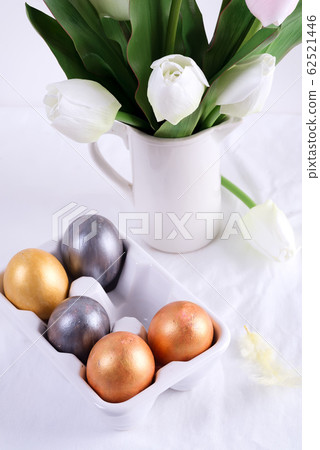 Golden Easter Eggs in ceramic egg tray with tulip on white table. Easter background or easter concept. Golden Easter Eggs in ceramic egg tray with tulip on white table. Easter background or easter concept. 62521446