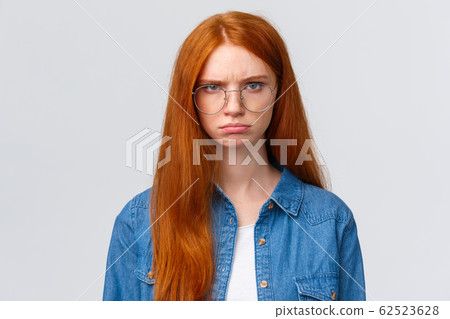 Close-up portrait strict and angry, mad gloomy redhead girl staring offended and disappointed, pouting frowning outraged, condemn something, look skeptical and bothered white background 62523628