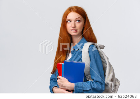 Creative and thoughtful cute daring foxy girl with red hair, hold backpack and notebooks, biting lip looking up pondering, want skip class and have fun friends, thinking over white background 62524068