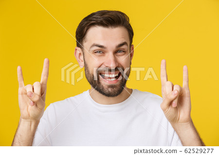 Young caucasian man wearing casual white t-shirt over yellow isolated background shouting with crazy expression doing rock symbol with hands up. 62529277