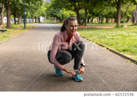 Female jogger tying her shoe laces in the park Female jogger tying her shoe laces in the park 62531556
