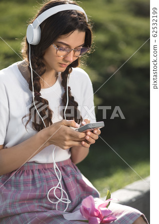 Woman With Smartphone and Headphones Outdoors in the City Park Woman With Smartphone and Headphones Outdoors in the City Park 62532199