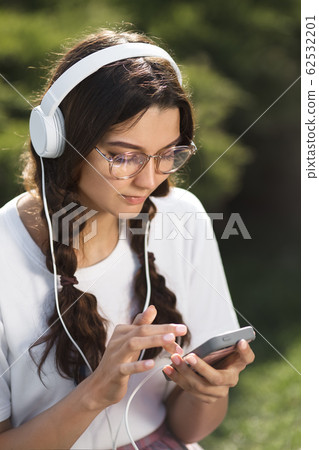 Woman With Smartphone and Headphones Outdoors in the City Park Woman With Smartphone and Headphones Outdoors in the City Park 62532201