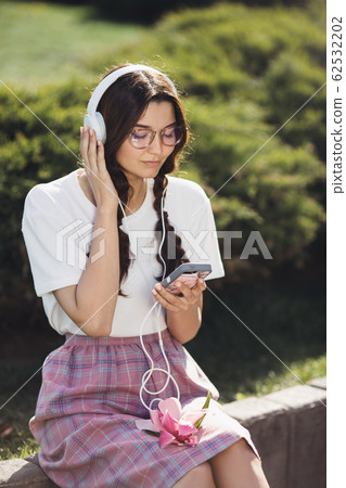 Woman With Smartphone and Headphones Outdoors in the City Park Woman With Smartphone and Headphones Outdoors in the City Park 62532202