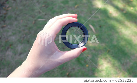 A hand holding a close-up lens, with green lawn in the background. A hand holding a close-up lens, with green lawn in the background. 62532223